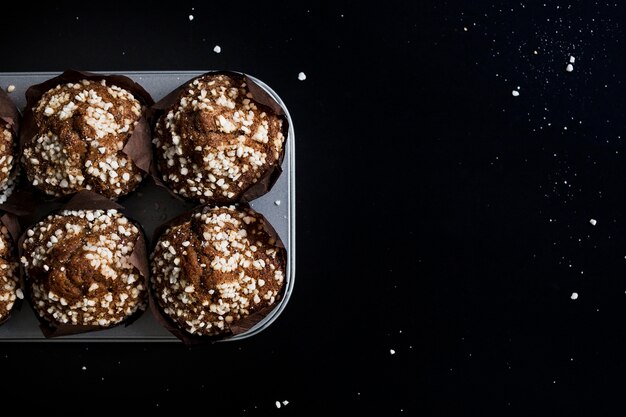 Chocolate muffins in paper cupcake holder on baking tray against black backdrop