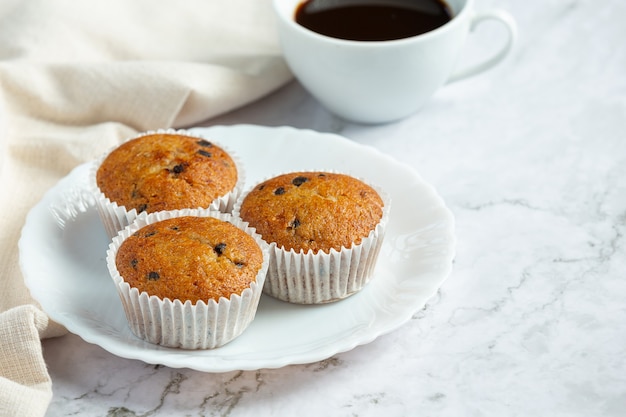 Chocolate muffins put on round white plate with a cup of coffee
