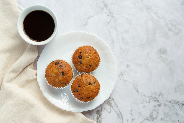 チョコレートマフィンは一杯のコーヒーと丸い白いプレートに置かれます