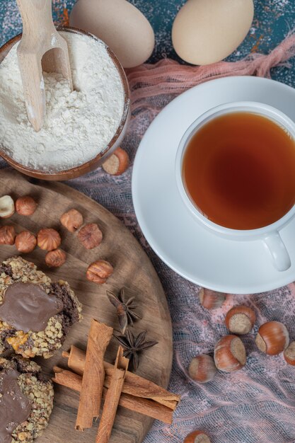 Chocolate nuts cookies on a wooden board served with cinnamons and a cup of tea.