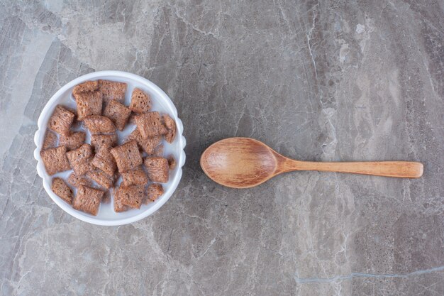 Chocolate pads corn flakes in white bowl with a wooden spoon . 