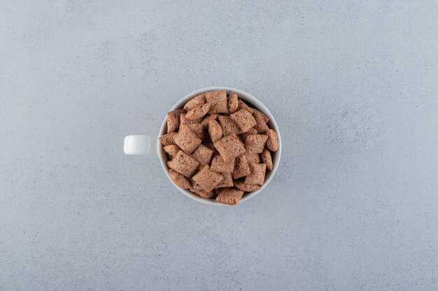 Chocolate pads cornflakes in ceramic mug on stone surface