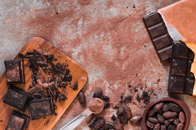 Chocolate pieces, bar and cocoa powder and beans bowls on messy table