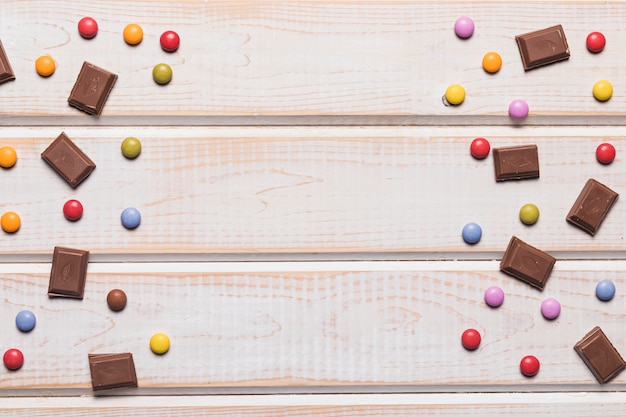 Chocolate pieces and colorful gems on wooden textured backdrop with copy space for writing the text