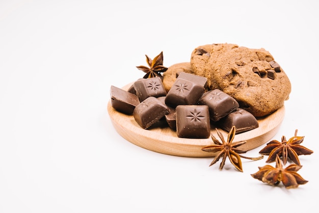Chocolate pieces and cookies with star anise on wooden frame against white background