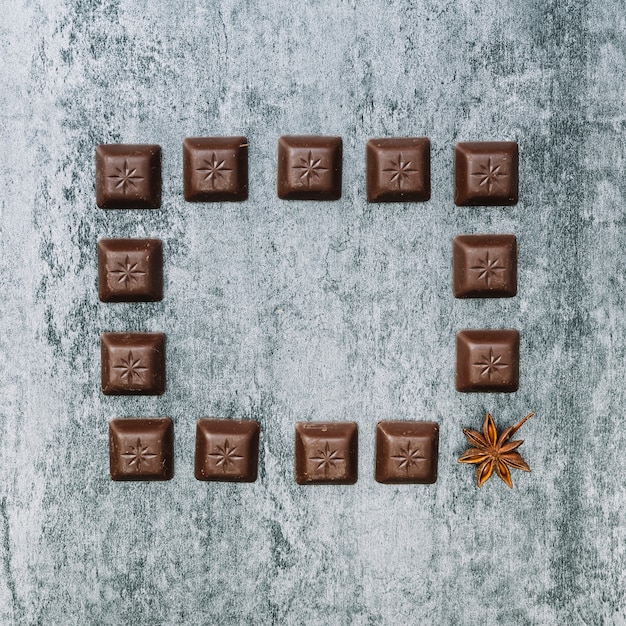 Free photo chocolate pieces frame with one star anise on an old wall