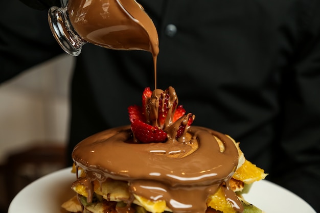 Chocolate pouring on pancakes banana strawberry nuts