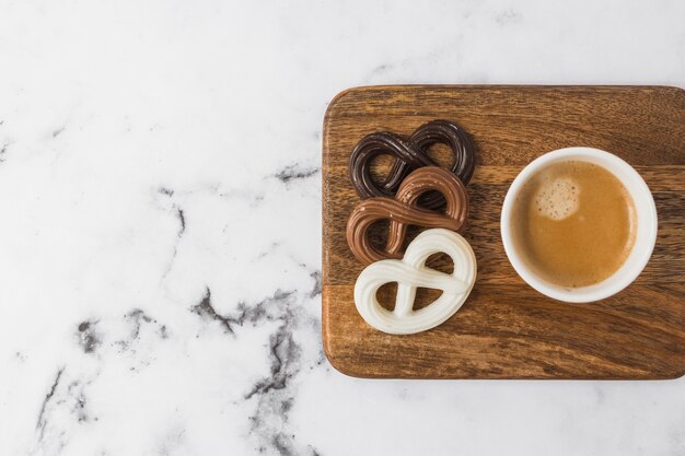 Chocolate pretzels and coffee cup on chopping board over marble textured background