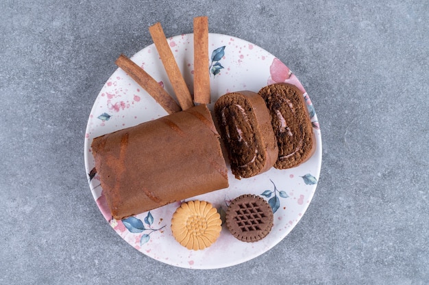 Chocolate roll cake, biscuits and cinnamon sticks on colorful plate