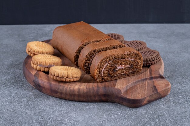 Chocolate roll cake and biscuits on wooden plate