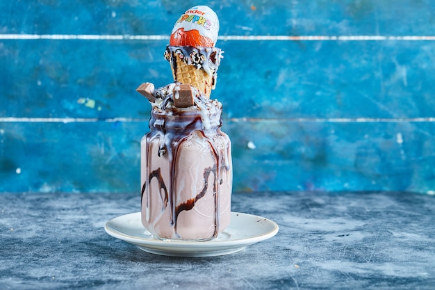 Chocolate smoothie with ice-cream cone, kinder surprise, chocolate syrup on the white plate in the blue surface