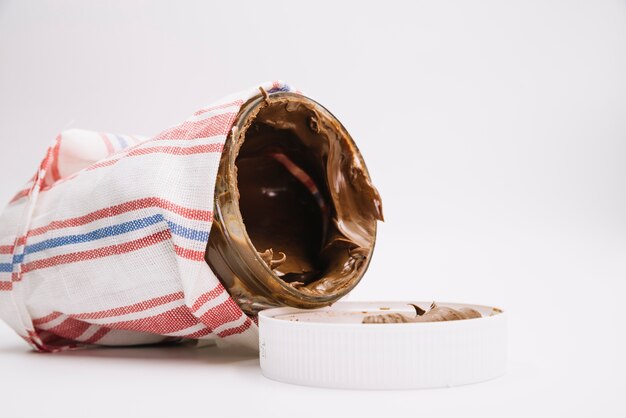 Chocolate spread jar wrapped in napkin with open lid on white background