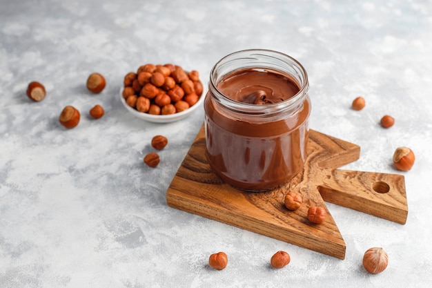 Chocolate spread or nougat cream with hazelnuts in glass jar on concrete ,  copyspace