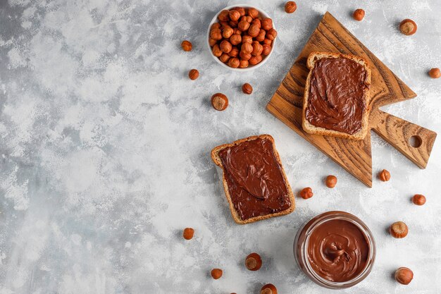 Chocolate spread or nougat cream with hazelnuts in glass jar on concrete ,  copyspace