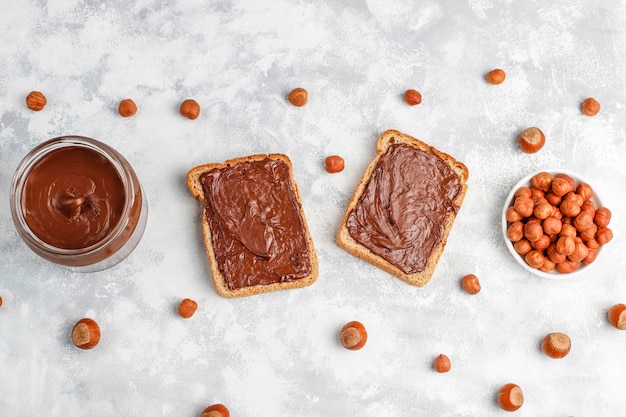 Free photo chocolate spread or nougat cream with hazelnuts in glass jar on concrete ,  copyspace