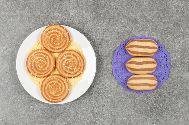 Chocolate striped biscuits on blue napkin with plate of sesame biscuits