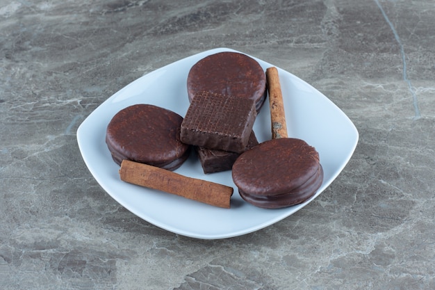 Chocolate wafer and cookies with cinnamon sticks on white plate.