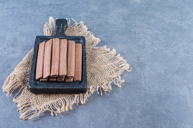 Chocolate wafer rolls in a board on a texture , on the marble background.