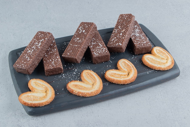 Бесплатное фото Шоколадные вафли и слоеное печенье на черной доске на мраморном фоне.