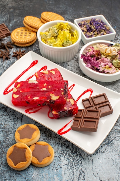 Free photo chocolate on white plate with bowls of dry flowers and cookies on grey ground