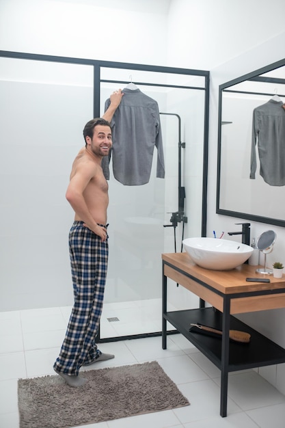 Choosing clothes. Man in plaid homewear holding a grey shirt