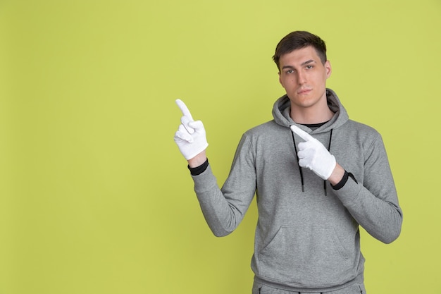 Choosing, pointing at side. Caucasian man's portrait isolated on yellow studio wall. male using gloves.