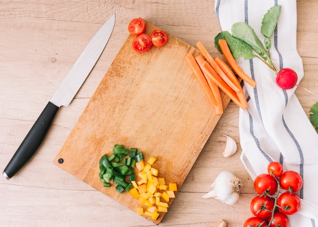 Chopped bell peppers; carrot; tomatoes; garlic bulb and turnip on wooden desk