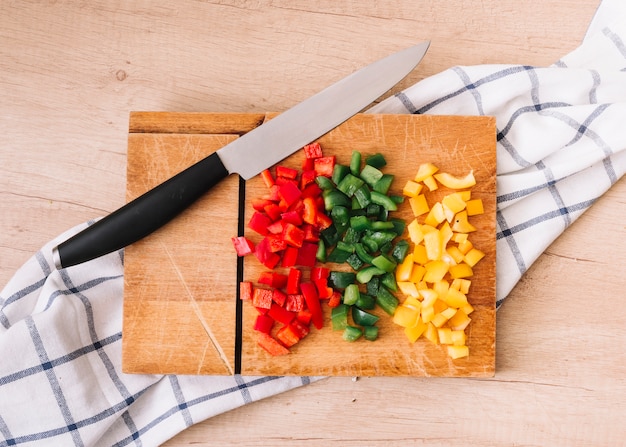 Free photo chopped bell peppers on chopping board with knife and tablecloth over the wooden table