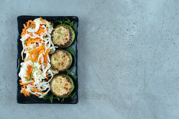 Chopped cabbage and carrots with grilled pepper on black plate.