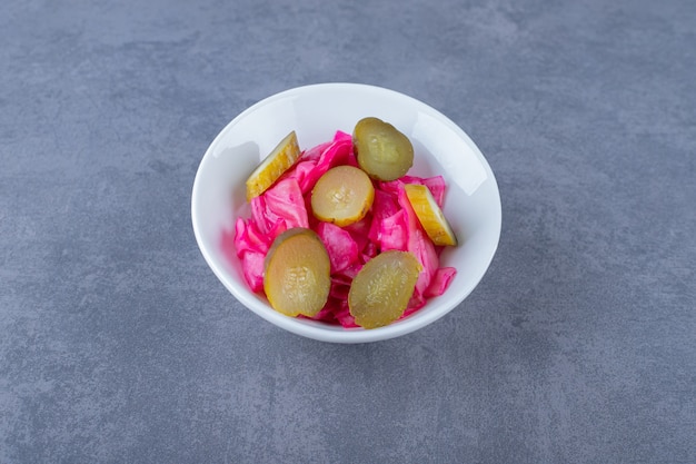 Chopped cabbage and sliced cucumber pickle in white bowl.