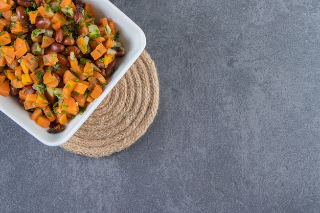 Chopped carrots and beans in a bowl on trivet on the marble surface