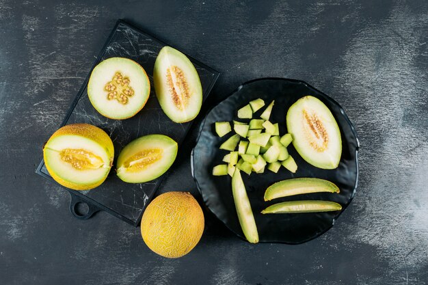 Chopped melon in a black bowl with split in half melon flat lay on a dark wooden background