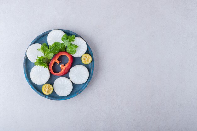 Chopped parsley, radish, pepper, kumquat on wooden plate, on the marble.