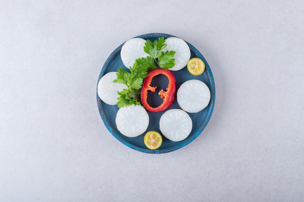 Chopped parsley, radish, pepper, kumquat on wooden plate, on the marble.