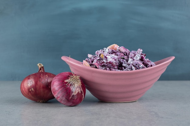 Нарезанный фиолетовый лук и салат из капусты в керамических чашках.