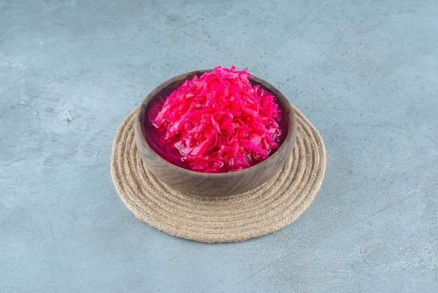 Chopped red fermented sauerkraut in a bowl on a trivet , on the blue table. 