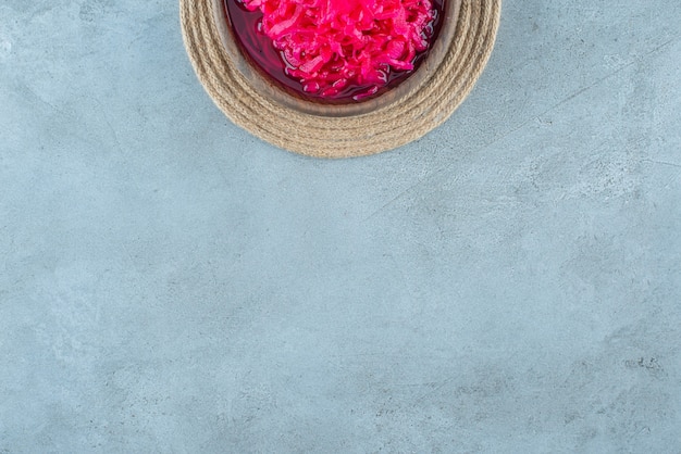 Free photo chopped red fermented sauerkraut in a bowl on a trivet , on the blue table.