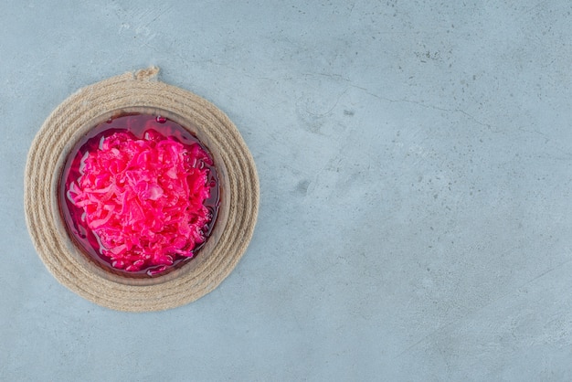 Chopped red fermented sauerkraut in a bowl on a trivet , on the blue table. 