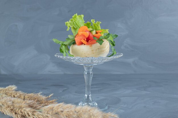 大理石のテーブルに針草の茎が付いたガラスの台座の白いカブの上に刻んだ野菜。