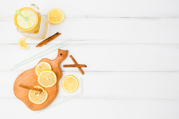 Chopping board with lemons near cinnamon and straws with glass