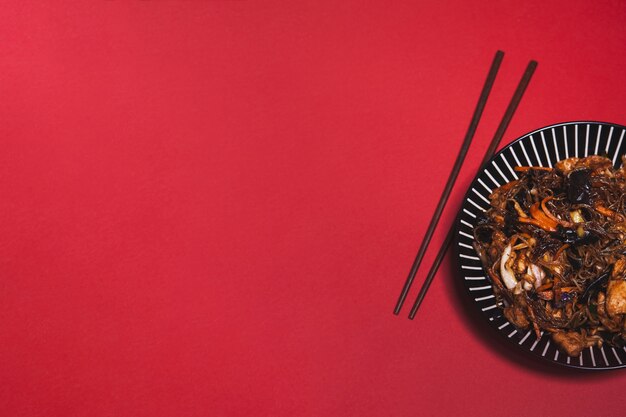 Chopsticks and Asian dish on red