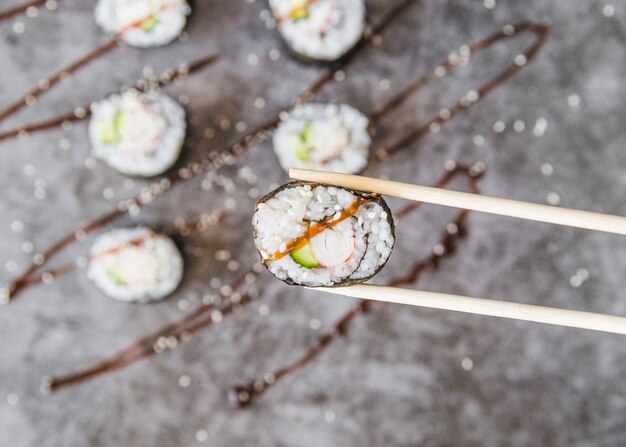 Chopsticks holding sushi roll with sauce 