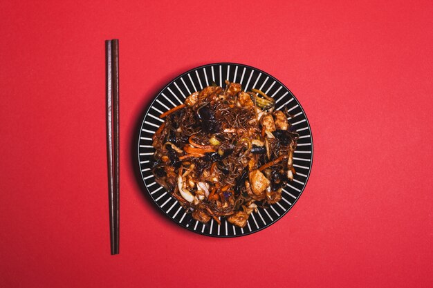 Палочки для еды возле тарелки с китайской едой