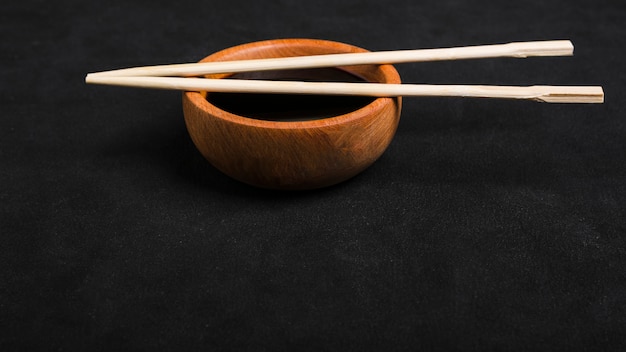 Chopsticks over the soya sauce wooden bowl on black backdrop