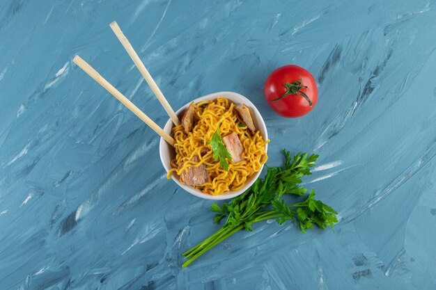 Chopsticks with meat noodles in a bowl next to parsley, on the marble background. 