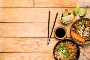 Free photo chopsticks with spring rolls; noodles and sauces with chopsticks on wooden table