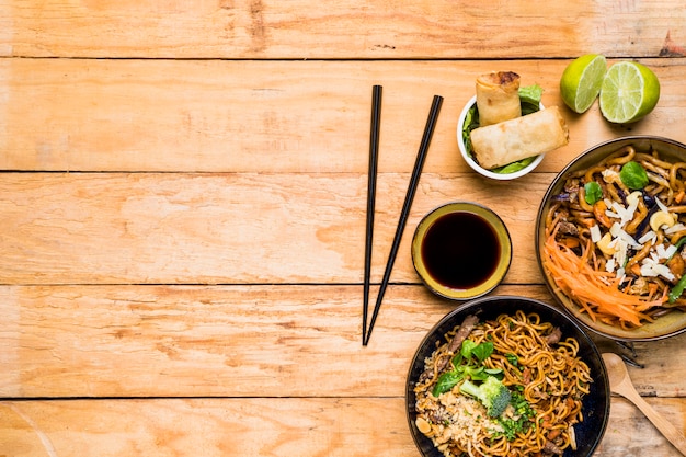 Chopsticks with spring rolls; noodles and sauces with chopsticks on wooden table