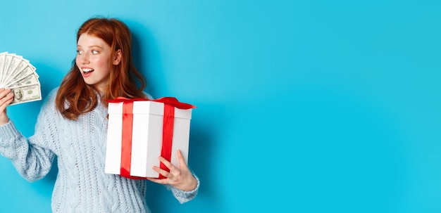 무료 사진 크리스마스와 쇼핑 개념은 큰 새해 선물을 들고 있는 달러를 보고 흥분한 빨간 머리 소녀