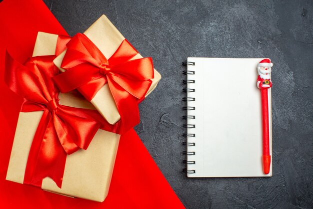 Christmas background with beautiful gifts with bow-shaped ribbon on a red towel and notebook with pen on a dark background