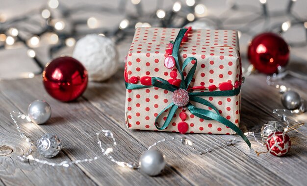 Christmas background with gift box close up on wooden surface, Christmas balls and bokeh lights.